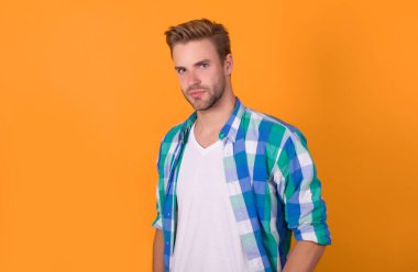 Yakışıklı görünüşüm benim malım. Yakışıklı bir erkek portresi. Genç adam sarı arka planda. Ciddi adam. Kareli tişörtlü havalı çocuk. Erkek yetişkin.