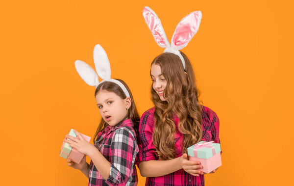 positive easter children in bunny ears hold gift box on yellow background.