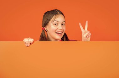 Boş turuncu kağıdın arkasında reklam için fotokopi alanı olan mutlu bir çocuk. Barış.