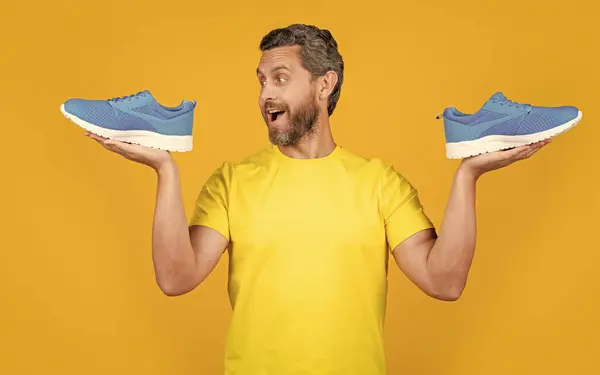 stock image image of amazed fitness man with sneakers shoes. fitness man with sneakers isolated on yellow. fitness man with sneakers on background. fitness man with sneakers in studio.