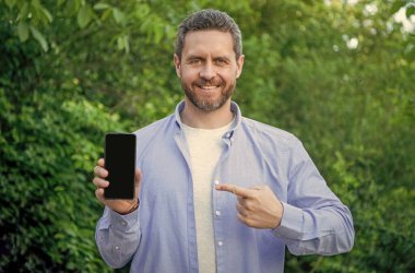 Akıllı telefon sunan adam, işaret parmağı. Adam dışarıda akıllı telefon sunuyor. Adam akıllı telefon ekranına kopyalama alanı sunuyor. Akıllı telefon sunan adamın fotoğrafı.