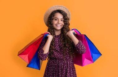 Kıvırcık saçlı mutlu kız sarı arka planda alışveriş torbaları tutuyor..