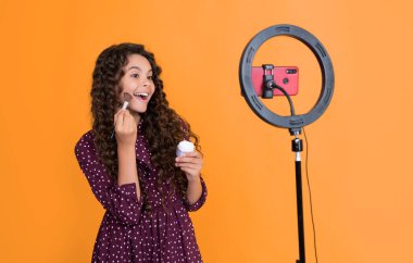 Uzun kıvırcık saçlı hayret bir çocuk blogda pudra fırçası için video çekiyor..