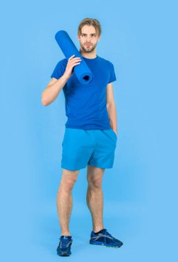 Yoga minderli sporcu stüdyoda bekliyor. Yoga minderli bir sporcunun fotoğrafı. Spor giyimli yoga minderli bir sporcu. Yoga minderli sporcu mavi arka planda izole edilmiş..