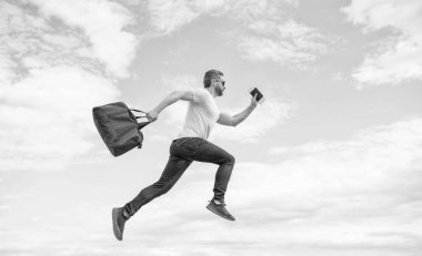 Energetic guy running with travel bag midair sky background, vacation.