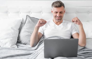 happy mature man working on laptop in bed.