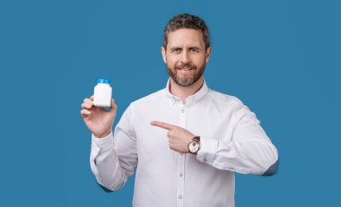 Adam stüdyodaki tedaviyi işaret ediyor. İlaç kavanozunu sunan adam. Elinde ilaç olan bir adamın fotoğrafı, sağlık hizmeti. Mavi arka planda ilaç tedavisi gören bir adam var..