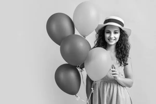 stock image photo of summer woman with balloons wearing hat, copy space. summer woman with balloons isolated on yellow. summer woman with balloons in studio. summer woman with balloons on background.