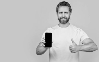 Stüdyoda akıllı telefon uygulaması gösteren bir adam, kopyalama alanı. Akıllı telefon uygulaması gösteren bir adamın fotoğrafı. Akıllı telefon uygulaması gösteren adam sarıda izole edildi. Adam arka planda akıllı telefon uygulaması gösteriyor.