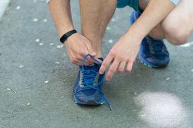 Sporcu antrenmana hazırlanıyor. Ayakkabılarını giyip yerde oturuyor. Spor ayakkabılarını bağlayan sporcu. Atletik ayakkabılar. Spor ayakkabısı kravat bağcıkları dışarıda. Spor ayakkabılarını bağlayan spor adamı. Yakın çekim..