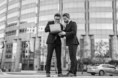 Çevrimiçi ticaret yapan iki iş adamını düşünüyorum. İş adamları açık havada ticaret yapıyor. İşadamları bilgisayarla online ticaret yapıyor. İnternet üzerinden ticaret yapan iş adamlarının fotoğrafı.