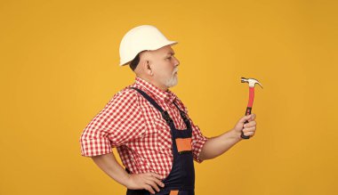 serious aged man carpenter in helmet on yellow background.