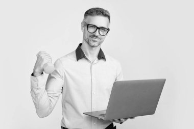 Gözlüklü gülümseyen olgun bir adam gri arka planda halterli bilgisayarla çalışıyor..