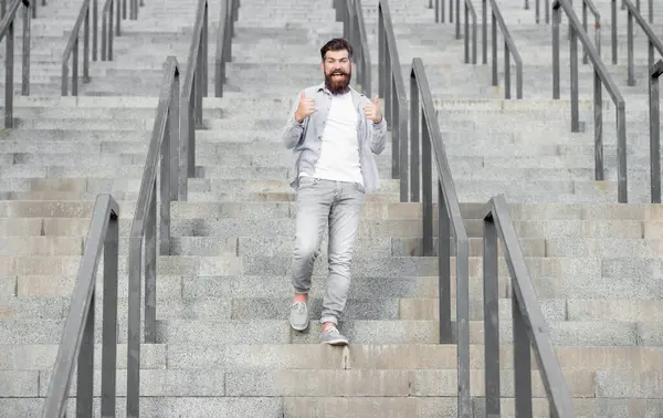 glad hipster walk downstairs. full length of hipster with beard. hipster man outdoor at stairs.