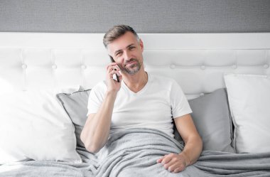 mature man smile in bed speaking on phone.