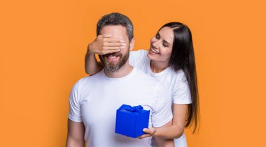 Kutusu olan neşeli bir tatil çifti. Bayram sürprizi için hediyeli bir çift fotoğrafı. Erkekler günü. Sarı arka planda sürpriz hediyeli çift var. Sürpriz çift.