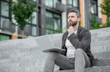 Bilgisayarlı serbest çalışan bir adam olduğunu düşünüyor. Bilgisayarlı serbest insan iletişimi. Serbest çalışma kavramı. Serbest çalışan adam dışarıda dizüstü bilgisayarda çalışıyor..