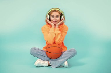 Basketbolcu kadının fotoğrafı müziği ve gülümsemeyi sever. Basketbolcu kadın mavi üzerine izole edilmiş müziği sever. Basketbolcu kadın stüdyoda müzik dinliyor. Arka planda müzik dinleyen basketbolcu kadın.