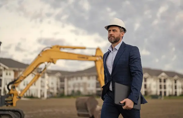 image of businessman with building plan wearing hardhat, copy space. businessman with building plan. businessman check building plan at site. businessman checking building plan outdoor.