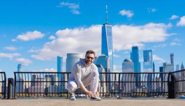 Atletik ayakkabılar. Spor ayakkabısı kravat bağcıkları dışarıda. Spor ayakkabılarının bağcıklarını bağlayan spor adamı. Sporcu antrenmana hazırlanıyor. Ayakkabılarını giyip yerde oturuyor. Spor ayakkabılarını bağlayan sporcu. Şehirde egzersiz yap..