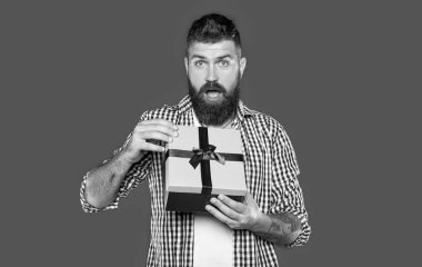 Gri arka planda hediye kutusu olan olgun sakallı adam şaşırdı..