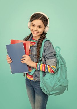 Happy teen girl listening to audio lesson blue background. Teenager listening to audiobook in headphones. Listening skills. School education.