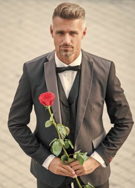 elegant man in tux. man wearing tux suit outside. hoary tux man with red rose.