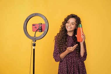 happy child with long frizz hair making video for blog hold shampoo.