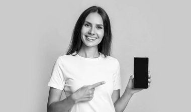 Mutlu kadın cep telefonunu işaret ediyor. Gülümseyen bir kadın mobil cihaz sunuyor. Mobil teknoloji. Mobil iletişim. Sunulan ürün, kopyalama alanı.
