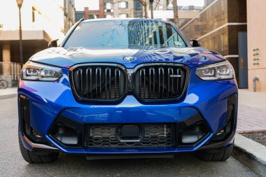 New York City, ABD - 25 Mart 2024: BMW X3 M parlak mavi araba açık havada park edilmiş, ön manzara.