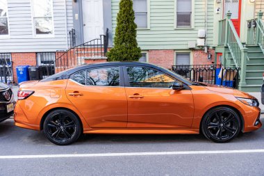New York City, USA - March 26, 2024: 2022 Nissan Sentra orange modern car parked outdoor, side view. clipart