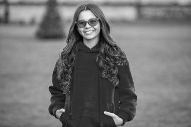 Neşeli şık genç kız gözlük takıyor. Şık bir genç kızın kapüşonlu giydiği bir fotoğraf. Açık havada şık bir genç kız. Şık bir genç kız..