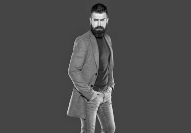 Sakallı yetişkin adam gri arka planda günlük giyiniyor..