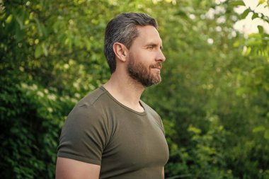 Tişörtlü sakallı adamın profil görüntüsü. Sakallı, beyaz bir adam. Olgun adam dışarıda..