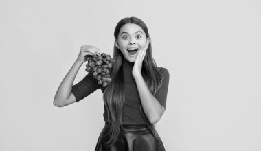 Şaşkın çocuk sarı arka planda bir demet üzüm tutuyor..