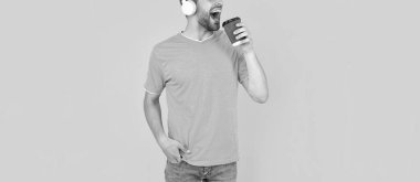 cropped unshaven young man in headphones drinking coffee on yellow background, lifestyle.