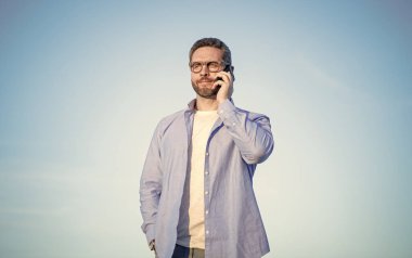 Cep telefonu çekiyor. Adam telefonda konuşuyor. Adam akıllı telefondan konuşuyor. Gökyüzü arka planında insan iletişimi.