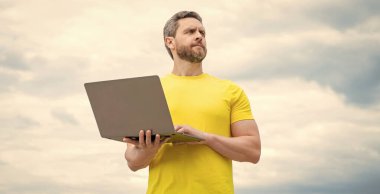 Gökyüzü arka planında dizüstü bilgisayarda çalışan serbest çalışan.