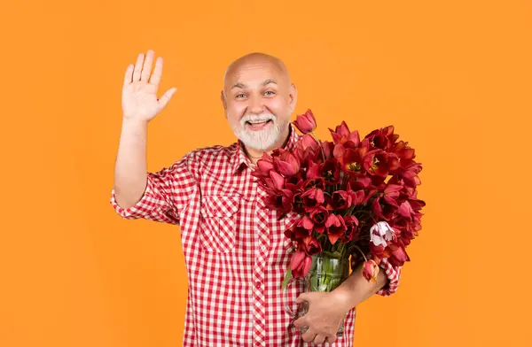 happy old bearded man hold spring tulip flowers on yellow background. hello.
