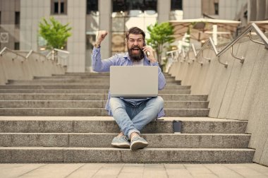 Mutlu adam cep telefonunda bağırarak kazanıyor. Kazanan merdivenlerde oturarak bahsi kazanır. İnternette bahis oynuyorum. Mobil bahis. Kazanmak için bahis.