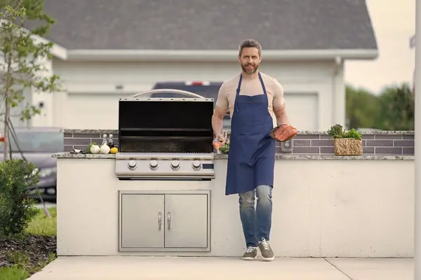 stock image photo of positive man cook seafood barbecue with fish. man cook seafood barbecue. man cook seafood barbecue outdoor. man cook seafood barbecue with salmon.