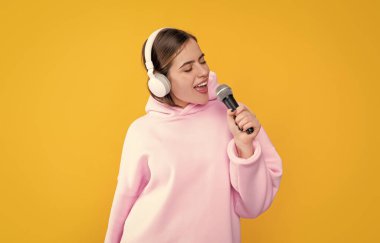 Sarı arka planda mikrofonu olan kulaklıklı genç bir kız..