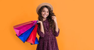 glad kid with curly hair hold shopping bags on yellow background.