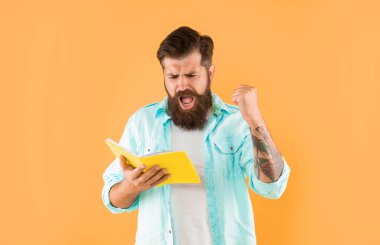 shouting hipster guy reading notebook on yellow background, success.