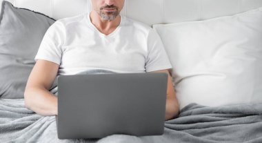 mature man working on laptop in bed. business online.