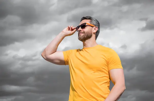 stock image man in yellow shirt and sunglasses outdoor on sky background. copy space.