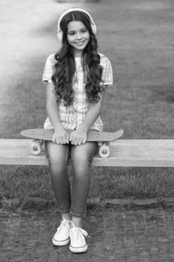 cheerful teen girl with skateboard in headphones. teen girl with skateboard outside. teen girl with skateboard listen music. teen girl with skateboard outdoor. clipart