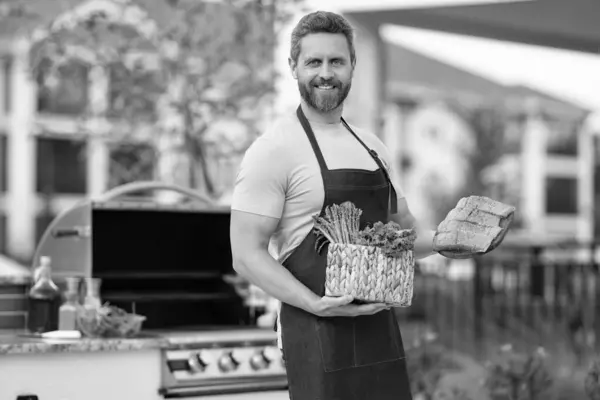 stock image cheerful barbecue man with salmon. barbecue man with salmon outdoor. barbecue man with salmon in apron. photo of barbecue man with salmon fish.