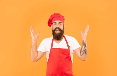 Excited chef man in toque and apron happy screaming with open arms yellow background, happiness.