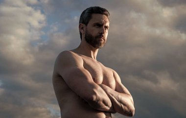 Üstsüz, kaslı adam. Kaslı gövdeli maço bir adam. Gökyüzündeki atletik adam.